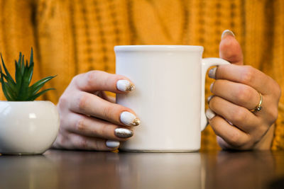 Close-up of woman with nail art holding coffee mug at table