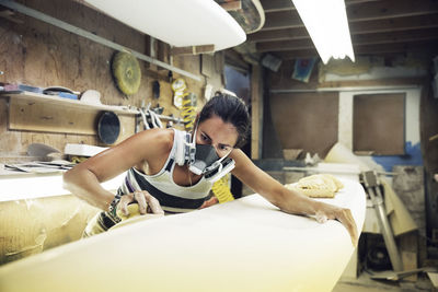 Woman shaping surfboard in workshop