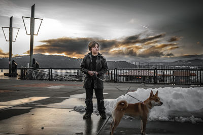 Portrait of man with dog standing against sky during sunset