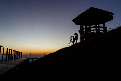 Silhouette hut on beach against clear sky during sunset