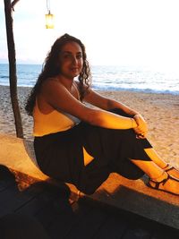 Portrait of young woman sitting on beach against sky