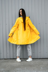 Girl in a yellow raincoat and gray jeans stands on a gray background. youth subculture