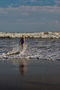 Rear view of girl in swimsuit standing at beach against sky