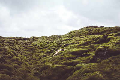 Low angle view of naked mid adult woman lying on mountain against cloudy sky