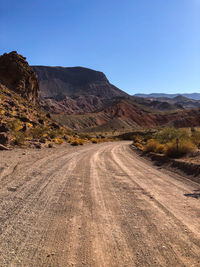 Dirt road amidst mountains against clear sky