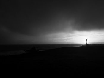 Silhouette lighthouse by sea against cloudy sky