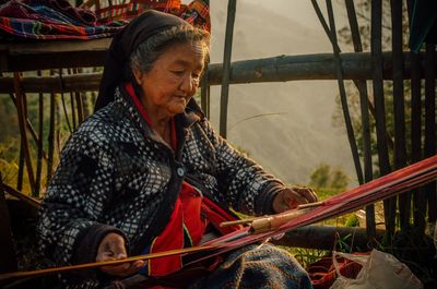 Senior woman weaving while sitting outdoors