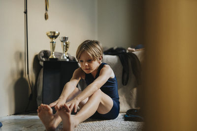 Elementary boy practices stretching exercise while sitting in bedroom