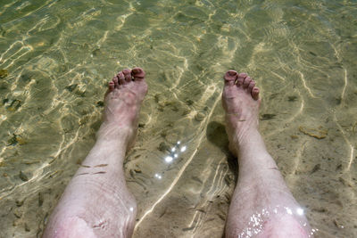 Low section of woman receiving fish pedicure in sea