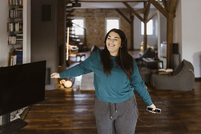 Carefree woman dancing while listening to music in living room at home