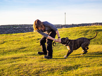 Full length of mature woman playing with dog on grass