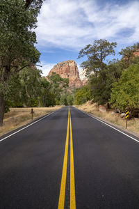 Empty road along trees and mountains against sky