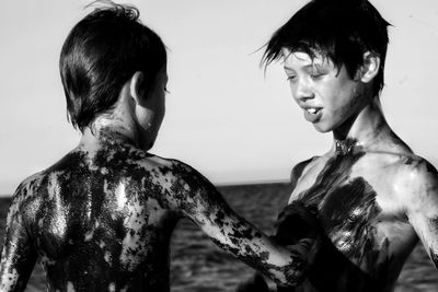 Boys in oil paint at beach against clear sky