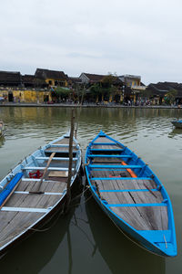 Boats moored in lake by buildings against sky