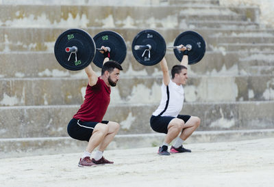 Two weightlifters lifting weights in an urban environment.