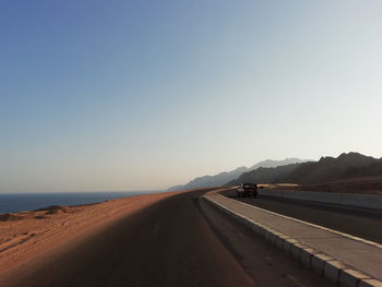 Road leading towards mountains against clear sky