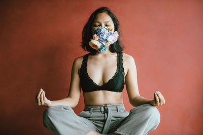 Woman wearing floral mask meditating while sitting against wall