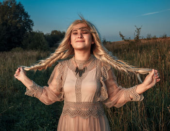 Smiling woman holding hairstyle hair against field