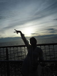 Full length of man standing by railing against sea during sunset