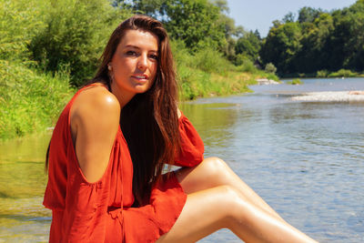 Portrait of smiling young woman sitting by water