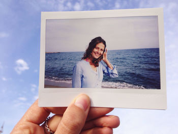 Cropped hand of person holding woman photograph against sky