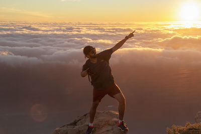 Full length of hiker posing while standing on rock against cloudscape