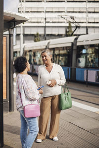 Smiling disabled woman talking with female friend while standing at train station