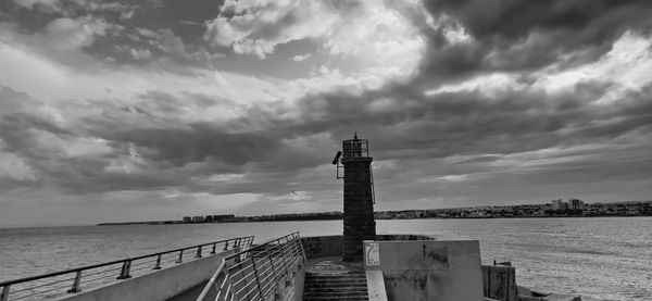 Lighthouse on pier over sea against sky