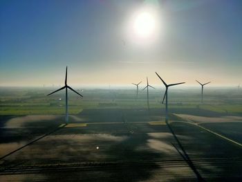 Windmills on landscape against sky on sunny day