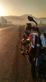 Motorcycle on road amidst field against sky during sunset