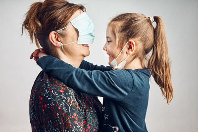 Little girl kissing her mother who has covered eyes with face mask for fun. daughter giving kiss