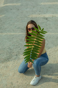 Portrait of young woman in sunglasses holding plant outdoors