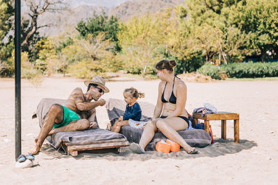 Girl sitting with parents on lounge chair at beach