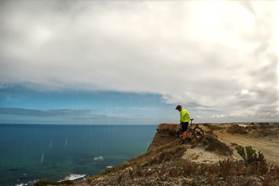 Rear view of man standing on rock by sea against sky