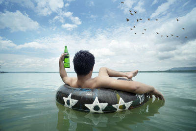 Midsection of shirtless man in sea against sky