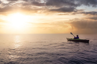 People in sea against sky during sunset