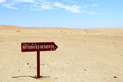 Sign board on sand against sky