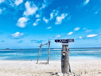 Information sign on wooden post at beach against sky