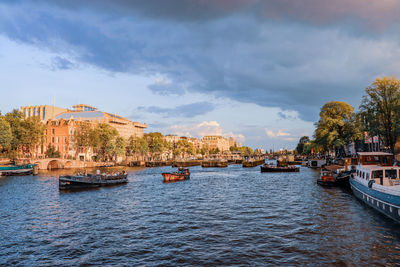 Boats in river by buildings in city against sky