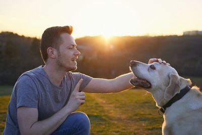 Young man sitting dog looking at sunset