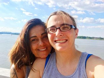 Portrait of happy friends at waterfront park against cloudy sky