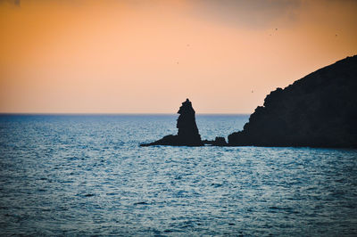 Silhouette rock in sea against clear sky during sunset
