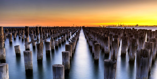 Wooden posts in sea against sky during sunset