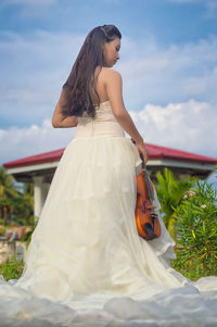 Rear view of bride holding violin while standing in front of gazebo