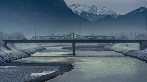 Bridge over snowcapped mountains against sky during winter