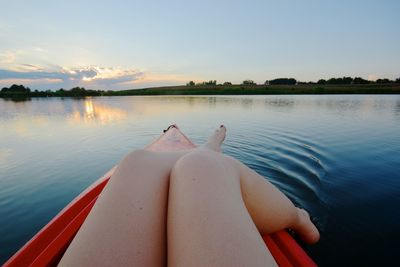 Low section of woman on kayak in lake against sky during sunset