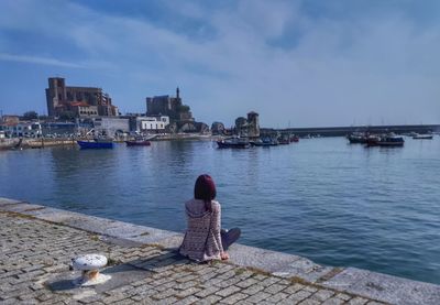 Rear view of woman sitting by sea against sky