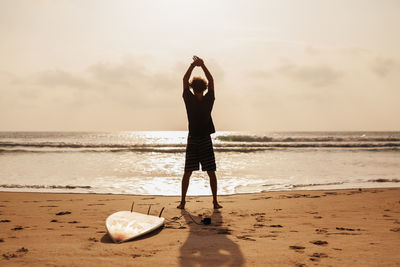 Surfer exercising on sand against sky during sunset