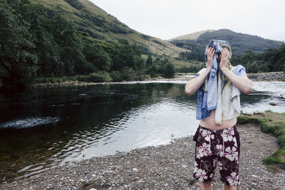 Man rubbing head while standing by lake