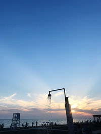 Silhouette people at commercial dock against blue sky during sunset